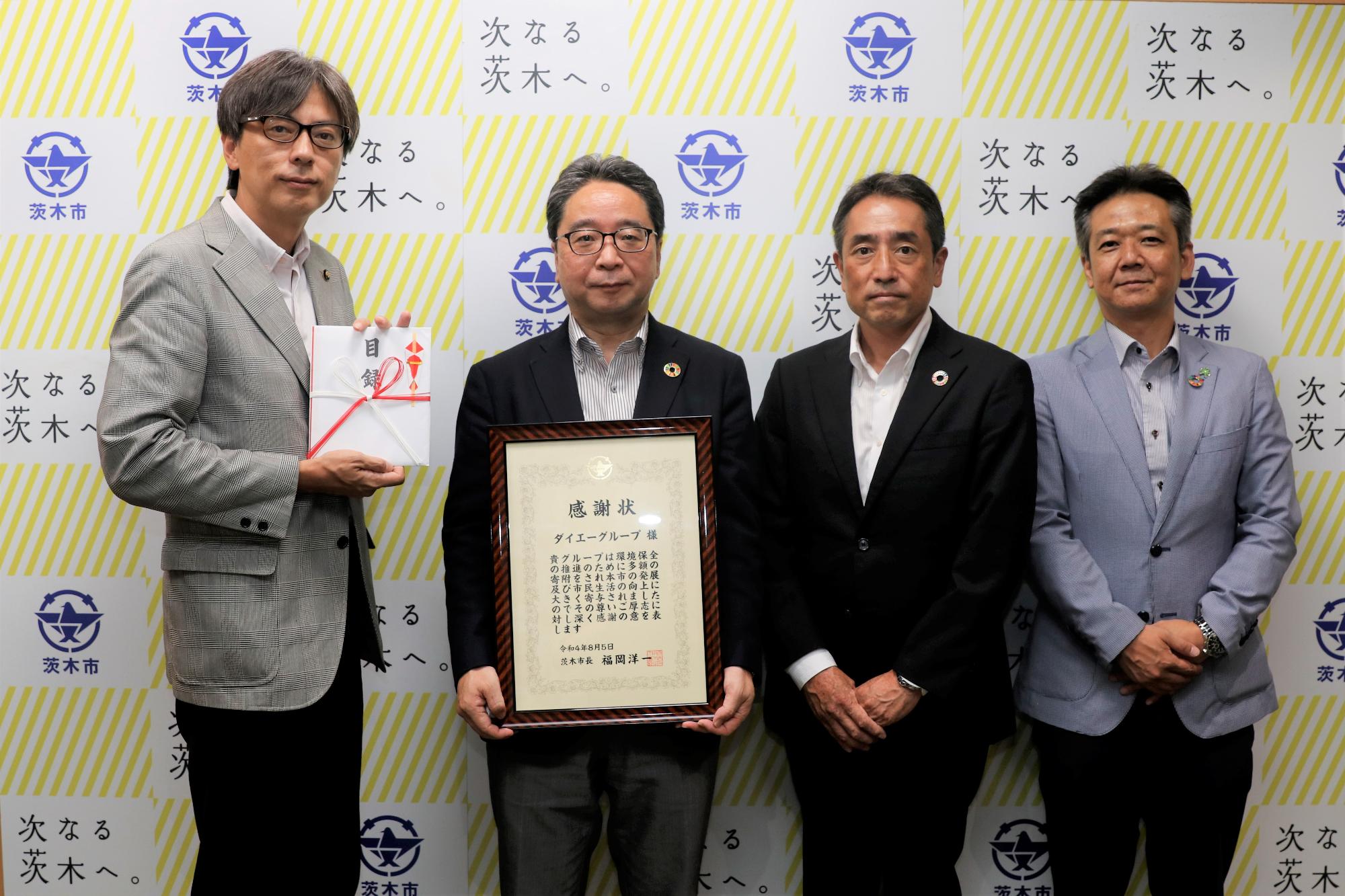 感謝状を持つ、おおたけ取締役、ふるかわ取締役、こだま部長と、目録を持つ市長の写真