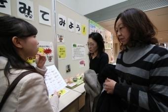 減塩の展示を見て説明を聞いている女性たちの様子