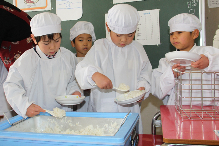 白いエプロン姿でご飯を配膳する園児たちの写真