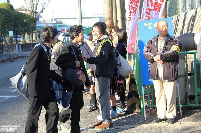 朝道路沿いであいさつを返す中学生や市民の写真