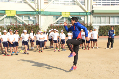 運動場で腕の振り方などを児童達に指導する冨岡耕児選手の写真