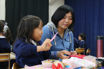 お弁当を一緒に食べる園児と学生の画像