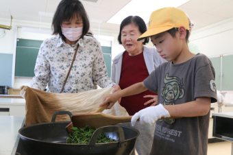 児童らが地域の方の指導を受けお茶の葉を煎っている写真