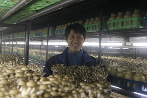 栽培室にて笑顔できのこを抱える中野稔さんの写真