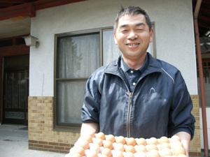 鶏卵のパッケージを持って笑顔を向ける清水洋さんの写真