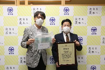 株式会社まるみつ様の隣でご寄付いただいたフェイスシールドを持つ市長の写真