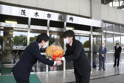 市役所東玄関の前で職員から花束を受け取る市長の写真