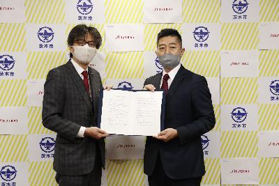 株式会社資生堂大阪茨木工場様と市長が協定書を持ち、並んでいる写真