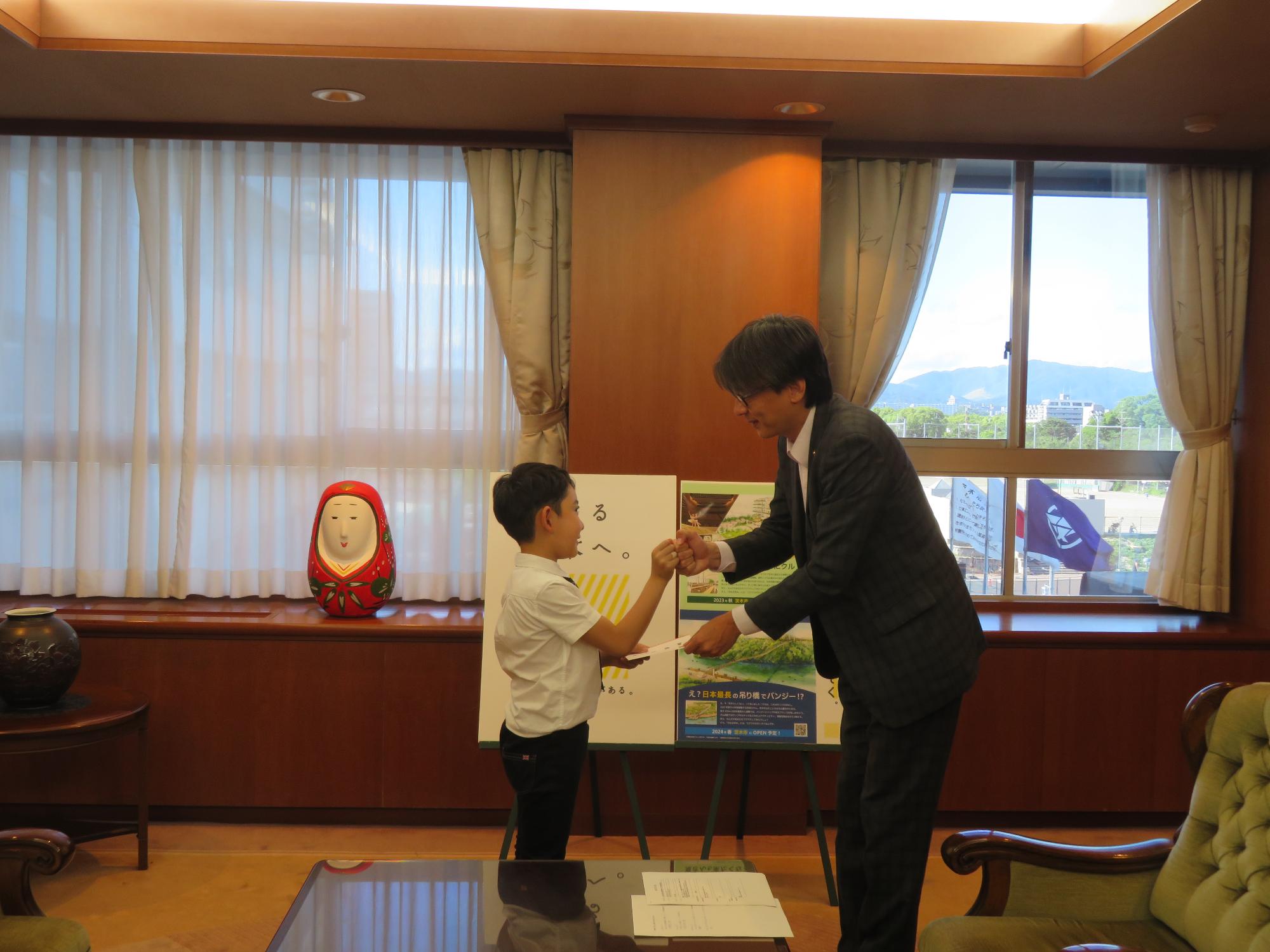 伊神拳一郎さんとグータッチをする市長の写真