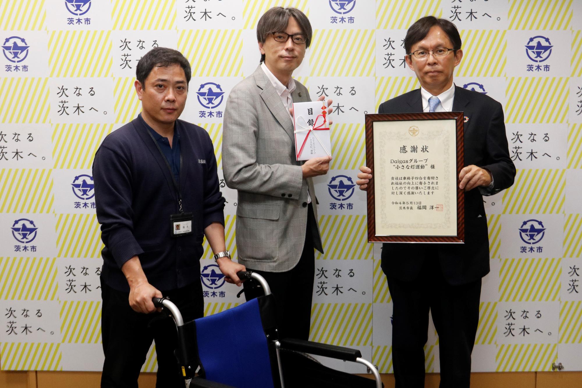 車椅子を持つ社会福祉協議会の職員と、感謝状を持つ大阪ガスネットワーク株式会社、ふくい支配人、目録を持つ市長の写真