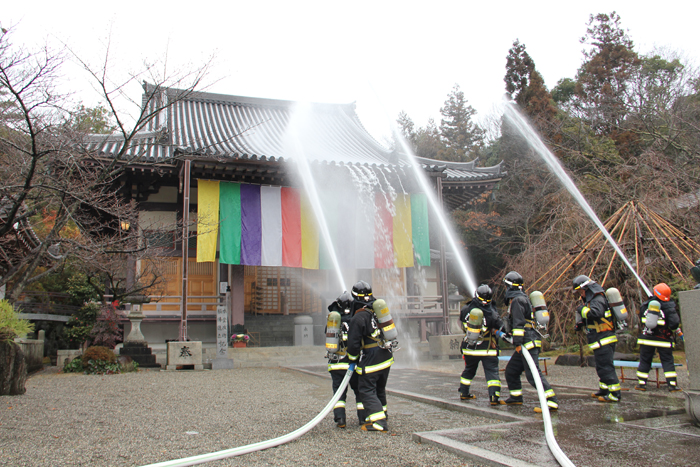 消防職員たちが本堂に向けてホースから放水をしている写真