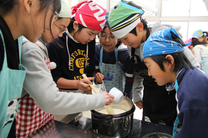 豆乳から豆腐を作る児童の写真