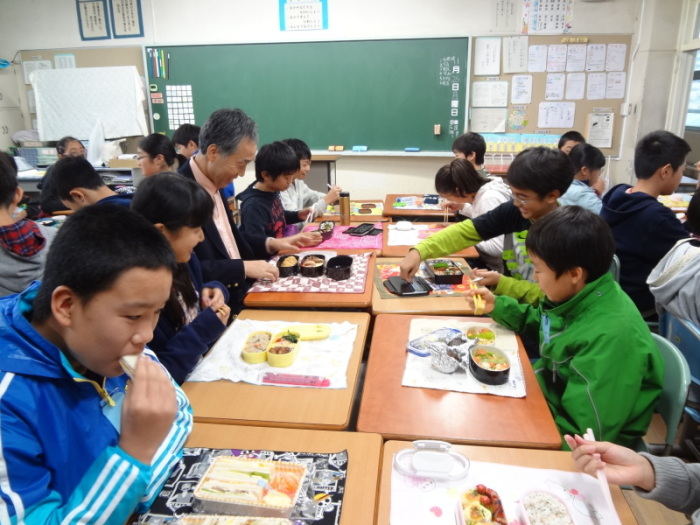 机をくっつけてみんなそろって自作のお弁当を食べる児童たちの写真