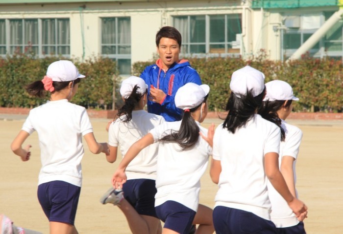 運動場で体を動かす児童と、指導する冨岡耕児選手の写真