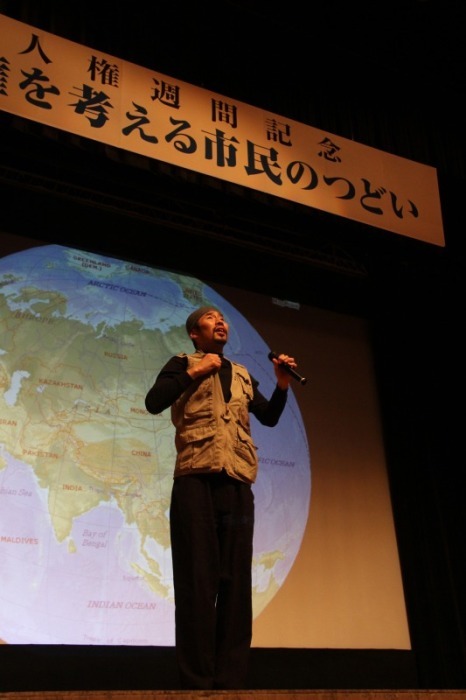 舞台上でマイクを持ち講演をする渡部陽一さんの写真