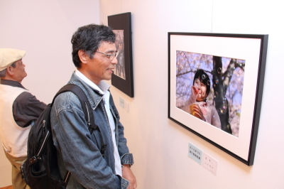 「市民さくらまつり」写真展でさくらまつり実行委員長賞に選ばれた作品を見る人の画像