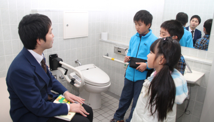 障害者用トイレを見学する児童らの写真