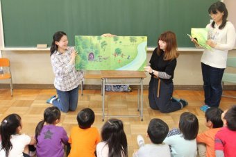 絵本を読む学生と真剣に聞く児童たちの画像