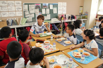 ガンバ大阪の選手と児童たちが一緒に給食を食べている画像