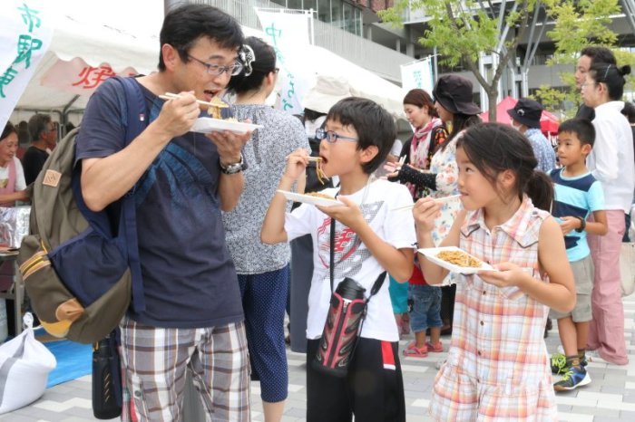 炊き出しの焼きそばをおいしそうに食べる親子の写真