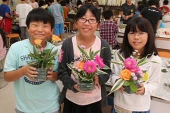 完成した生け花を誇らしげに見せる児童たちの写真