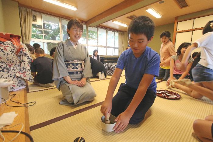 茶道の先生に笑顔で見守られながらお茶をたてる男子児童