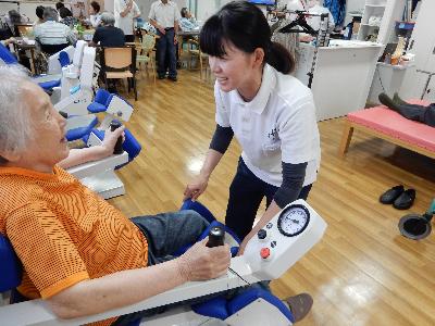 朝田さんが椅子型の器具で運動指導している写真